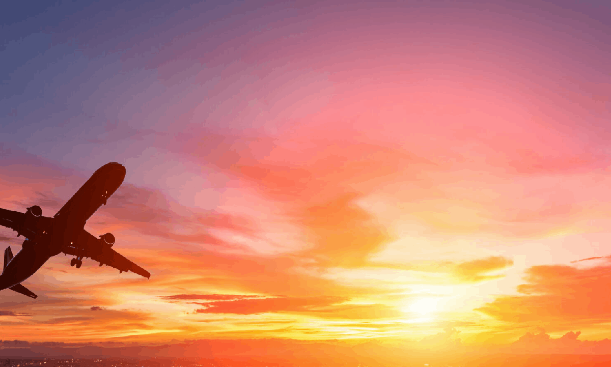 An aeroplane flying across a vivid orange and pink sunset sky.
